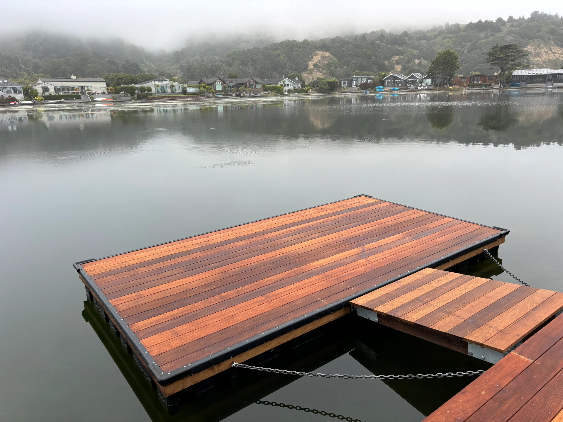 Newly built floating dock with hardwood decking, black bumper edging, and chain rigging on a West Marin lagoon