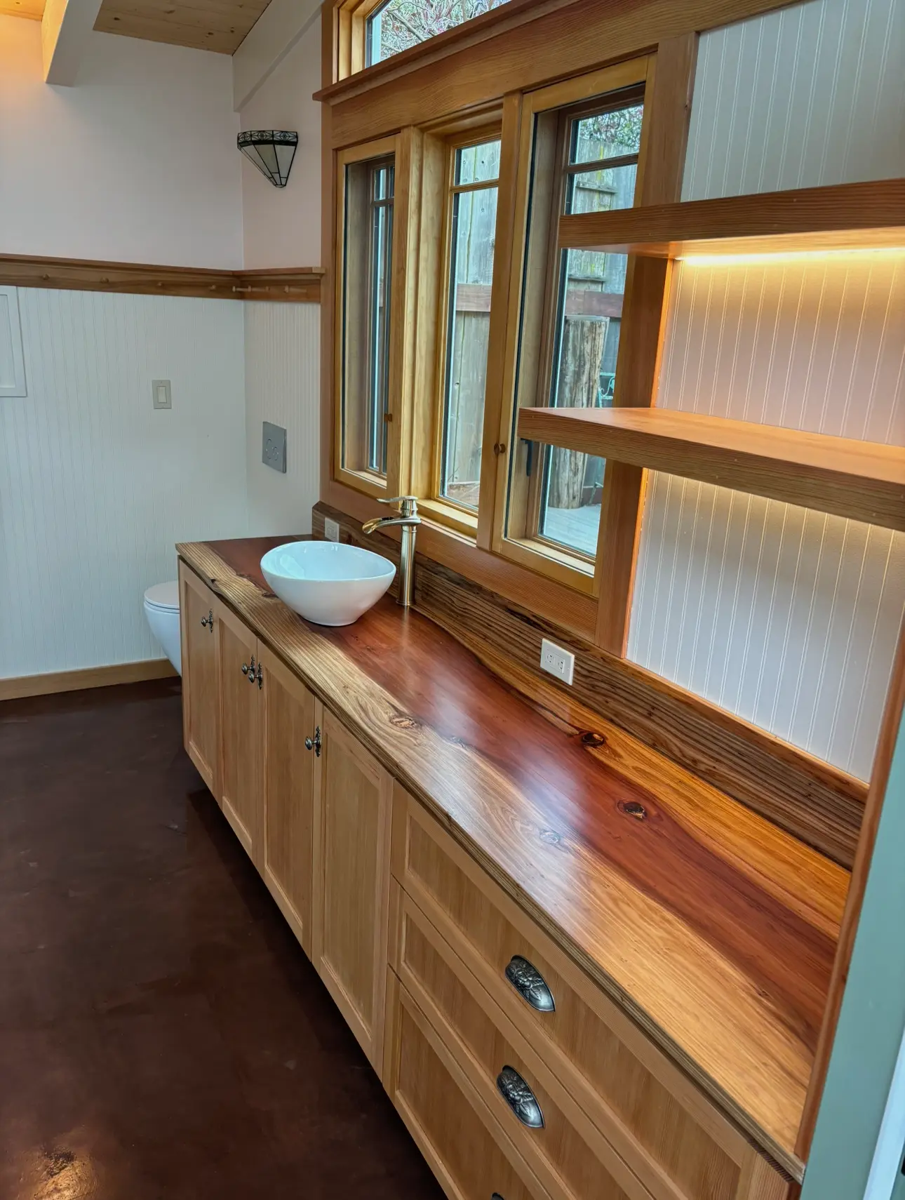 Bathroom with a natural wood vanity, vessel sink, custom shelves, and wood-trimmed windows