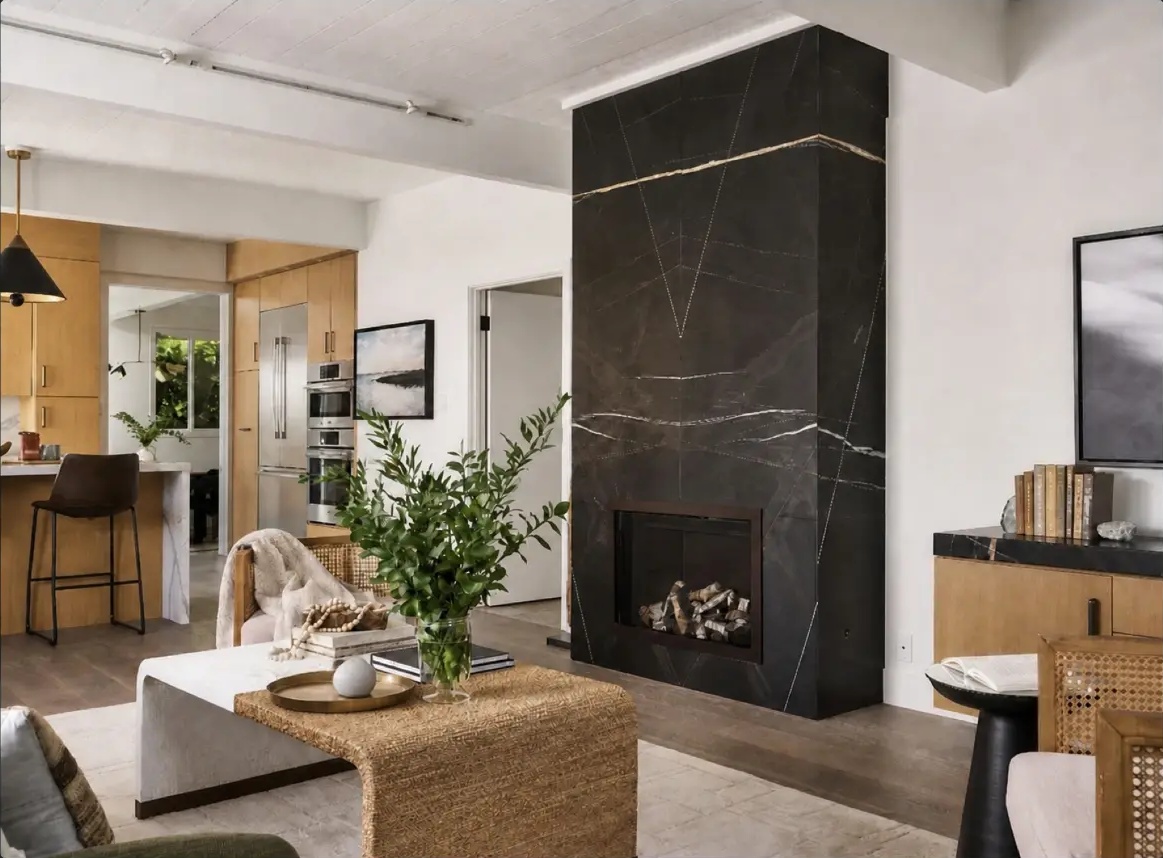 Living room with a floor-to-ceiling dark marble fireplace, wood cabinetry, and an open kitchen